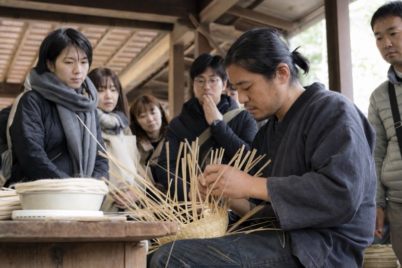 竹を編む作家の実演を見学する来場者