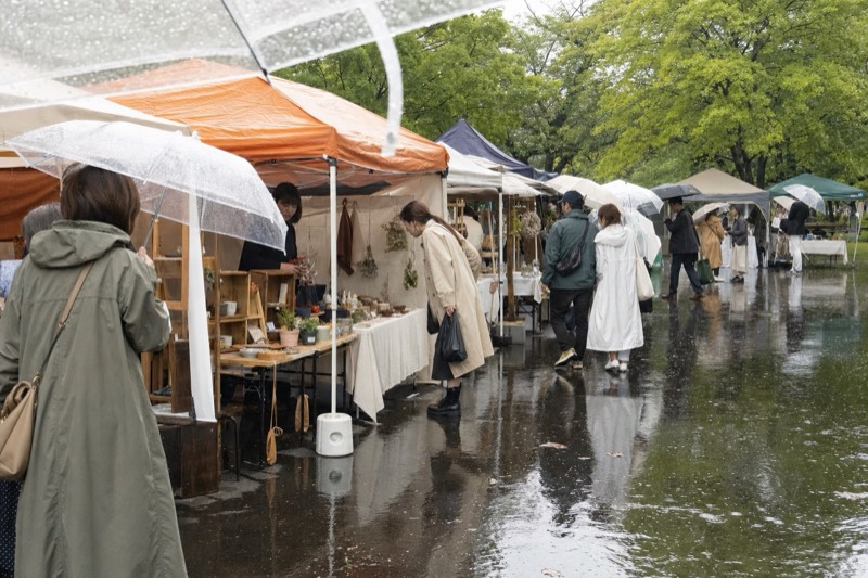 雨の屋外マーケットで傘を差して巡る来場者