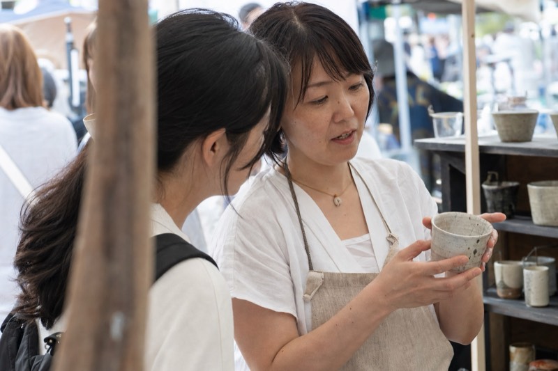 女性作家が来場者に陶器のカップを説明する様子